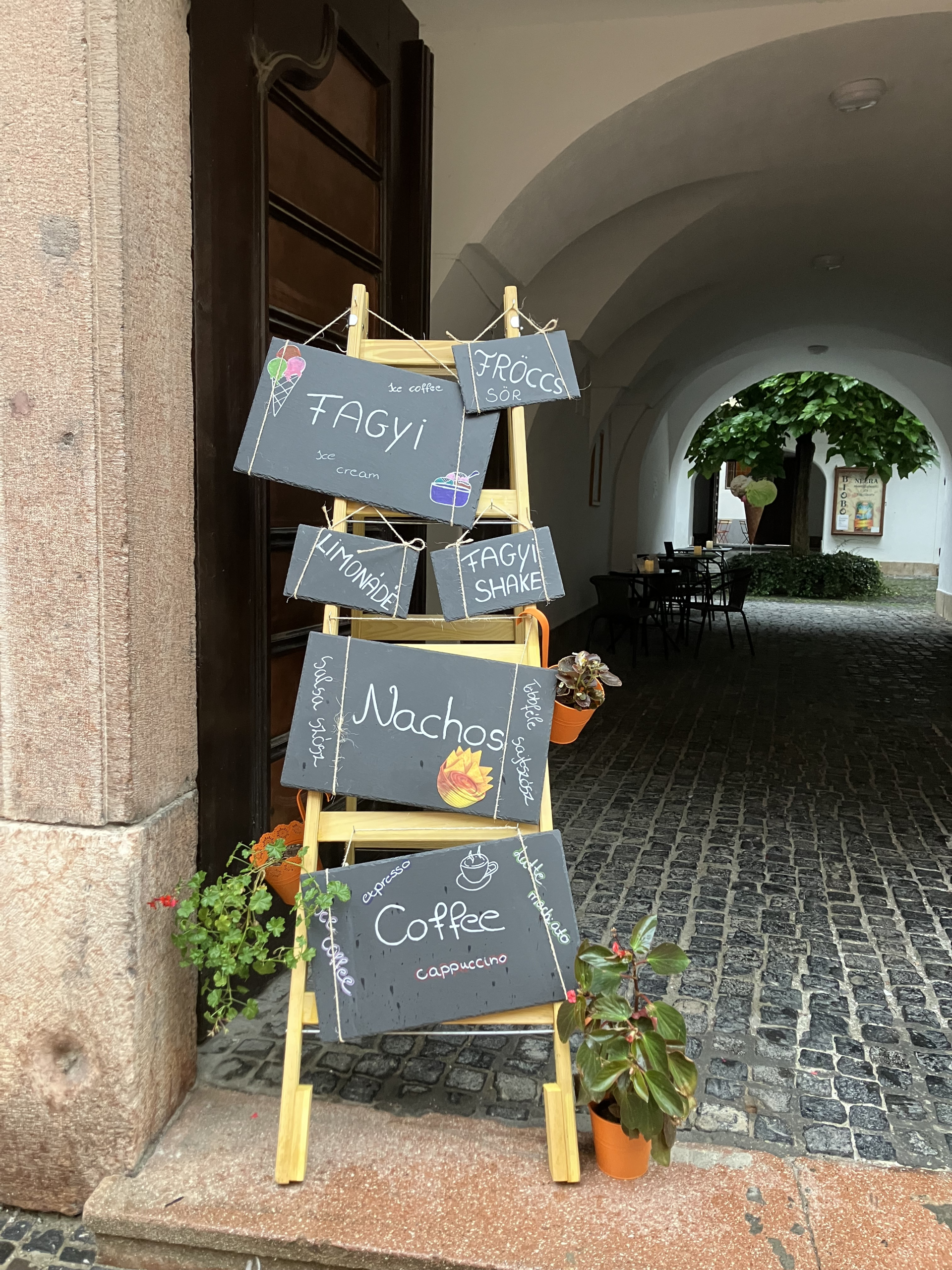 Kézzel írt kínálat-táblák a boltíves kapualjban